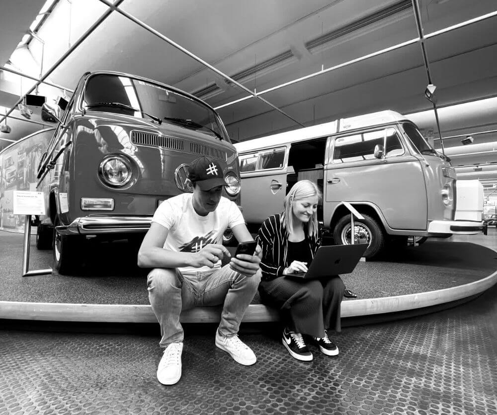 Agentur bartels. Inhaber Ingo Bartels und Mitarbeitende Vanessa Broistedt sitzen beim Kunden Automuseum Wolfsburg vor einem VW-Bus.